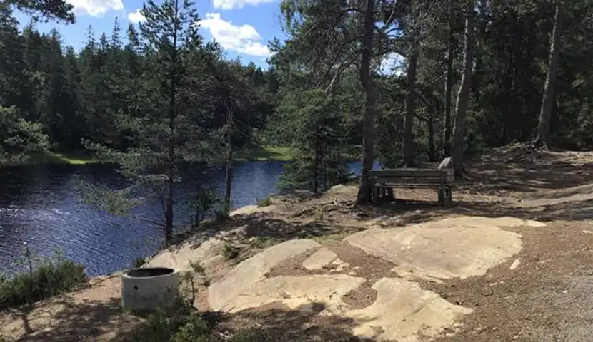 En benk og en bålplass ved siden av en innsjø.